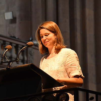 Eine junge Frau steht am Ambo im Altarraum des Mainzer Doms. Sie schaut gerade auf den vor ihr liegenden Text und schmunzelt leicht.
